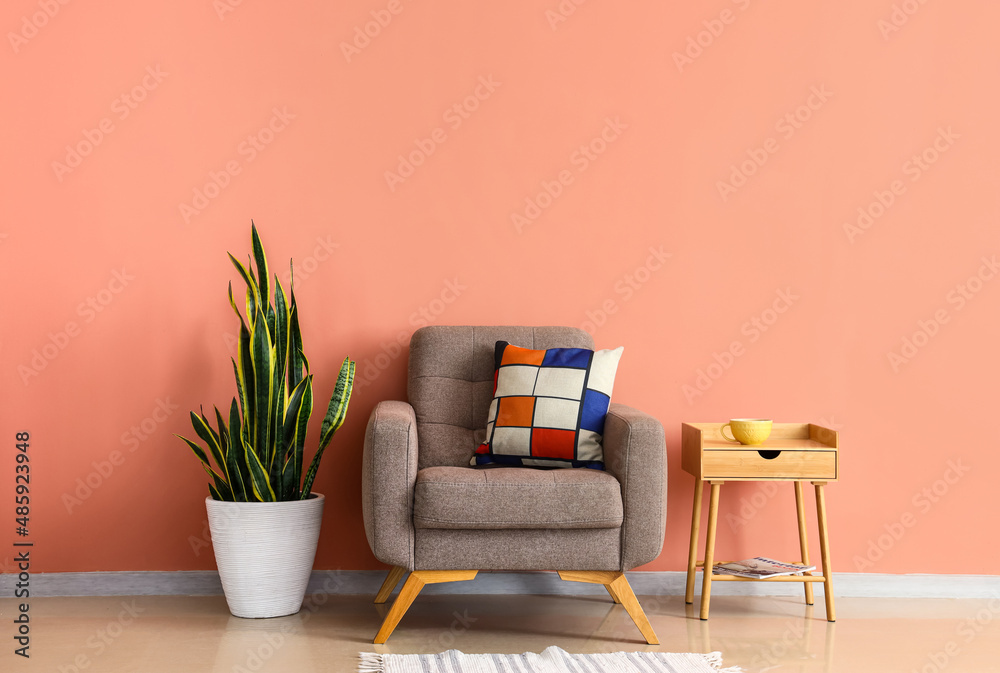 Wooden table with cup, soft armchair and houseplant near pink wall