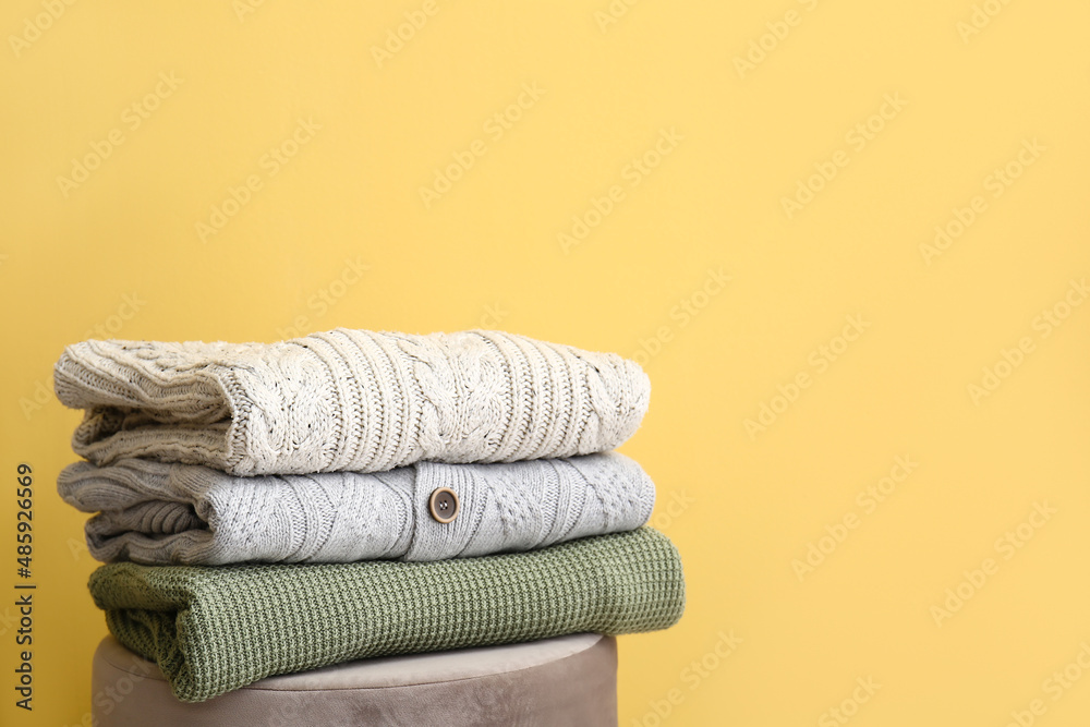 Warm sweaters on pouf near color wall