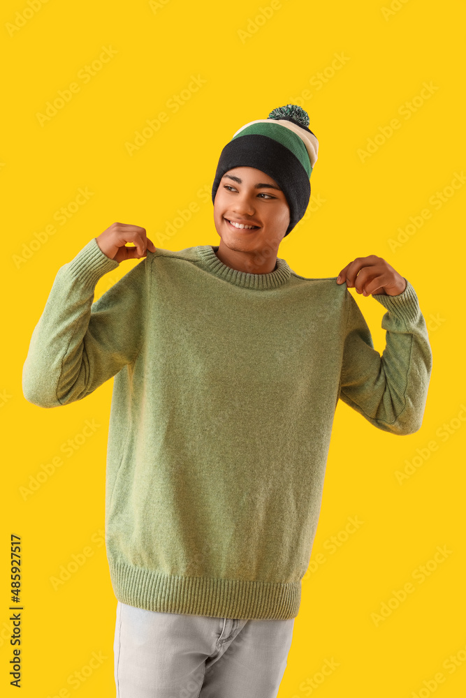 Handsome African-American guy in knitted sweater on yellow background