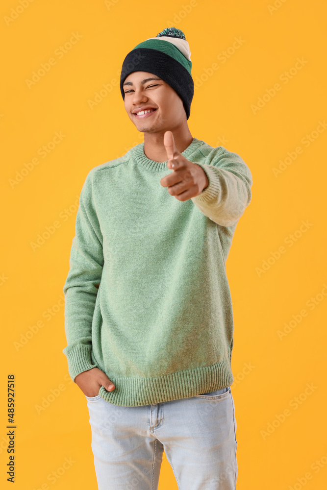 Handsome African-American guy in knitted sweater pointing at viewer on yellow background