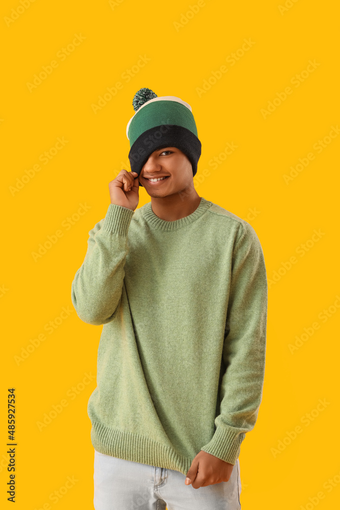 Handsome African-American guy in knitted sweater on yellow background