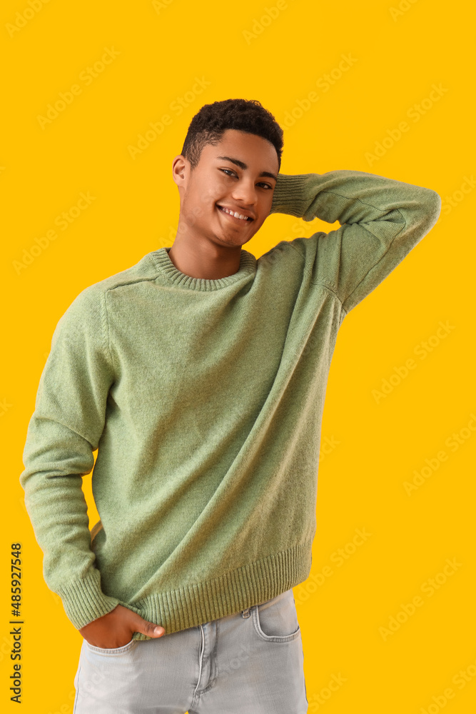 Handsome African-American guy in knitted sweater on yellow background