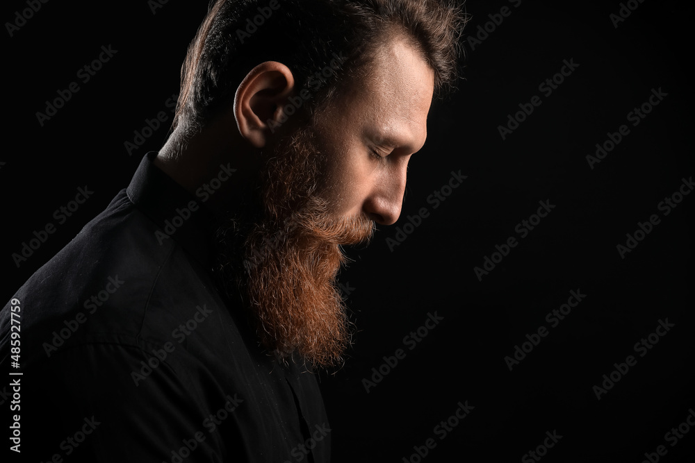 Calm young bearded man on black background