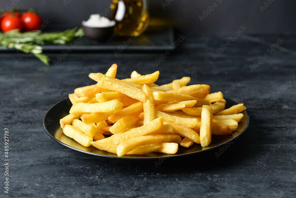 Plate with tasty french fries on black background