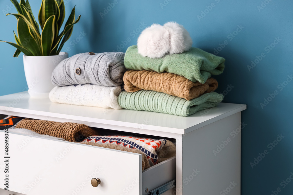 Stacks of stylish sweaters and opened drawer with warm clothes near color wall