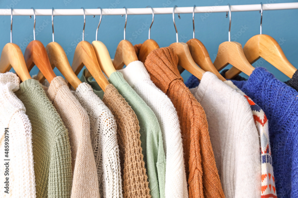 Closeup view of hangers with stylish knitted sweaters on color background