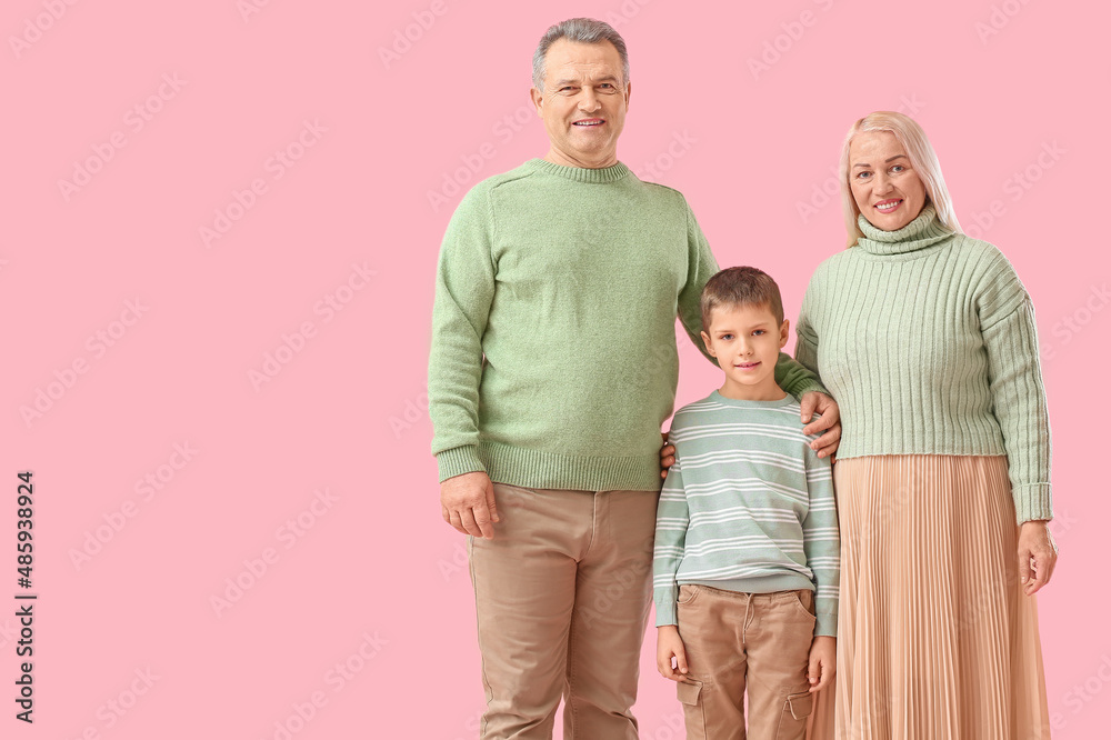 Little boy with his grandparents in warm sweaters on pink background