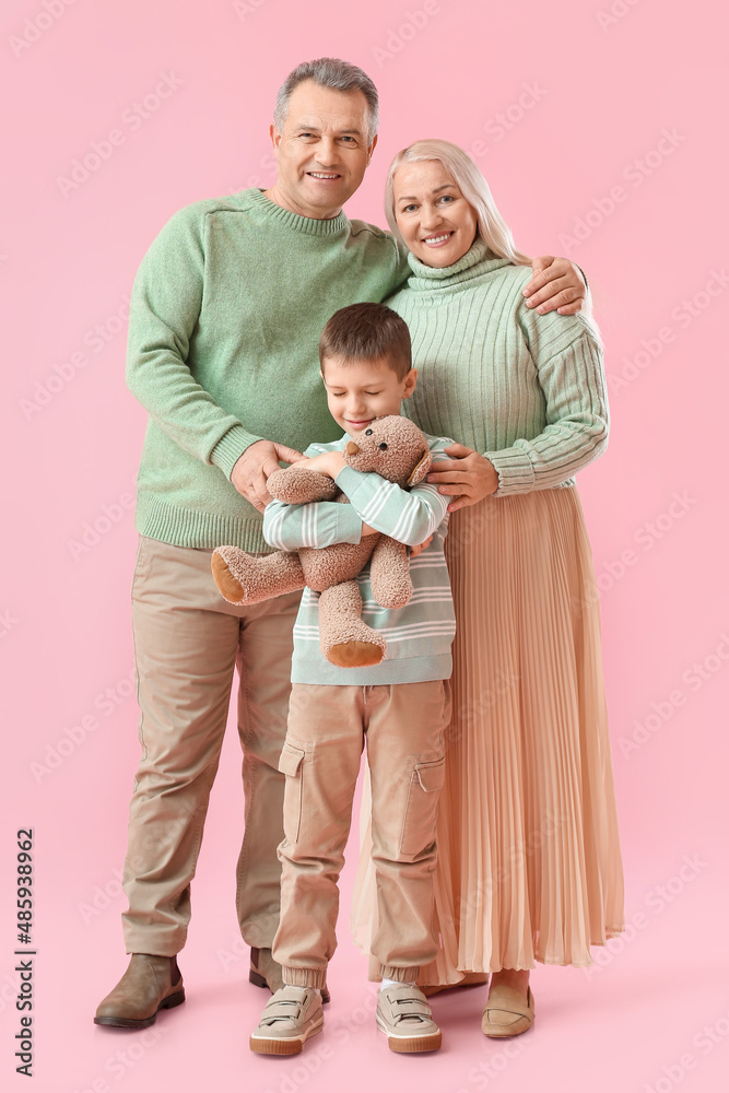 Little boy with toy and his grandparents in warm sweaters on pink background