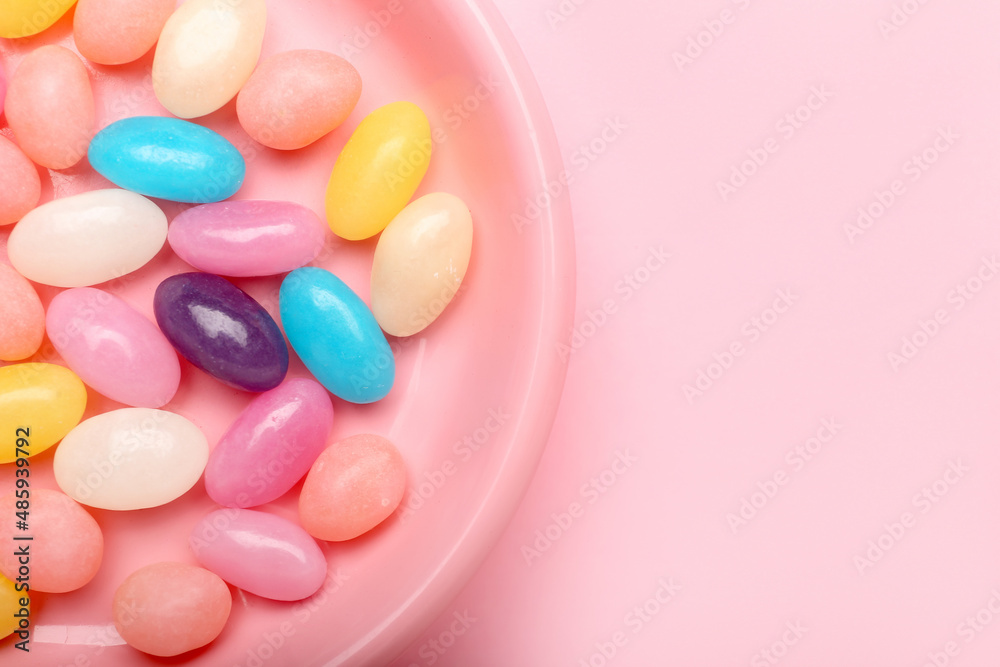 Plate with multicolored jelly beans on color background