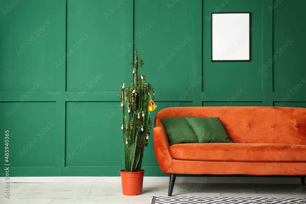 Cactus with Easter eggs and sofa near green wall