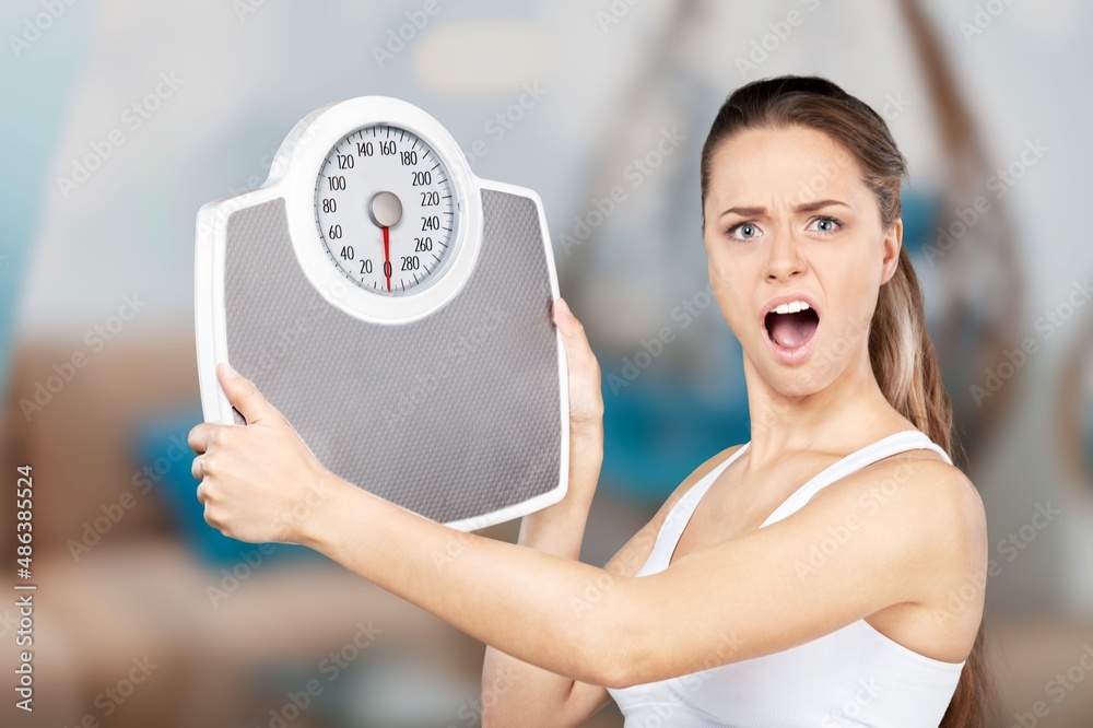 Young woman with scales bored of dieting Weight loss fail Upset on weight scale at home.