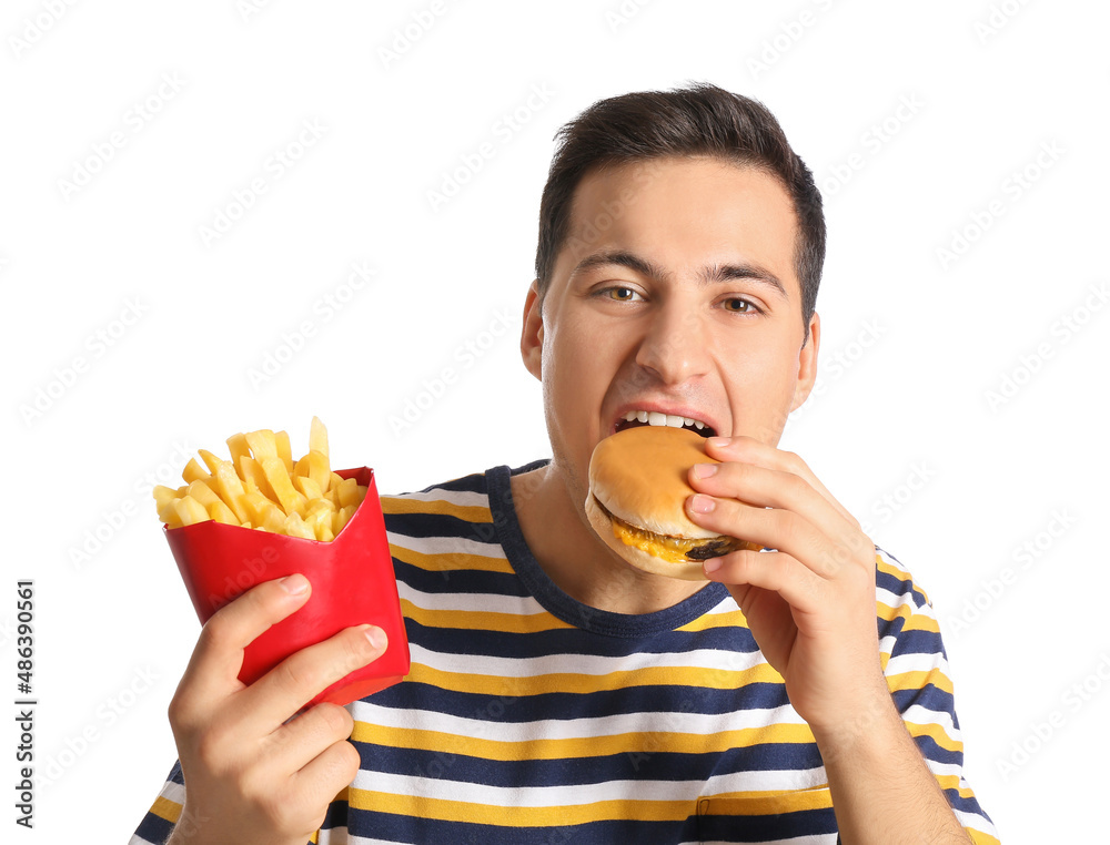 Young man with french fries eating burger on white background