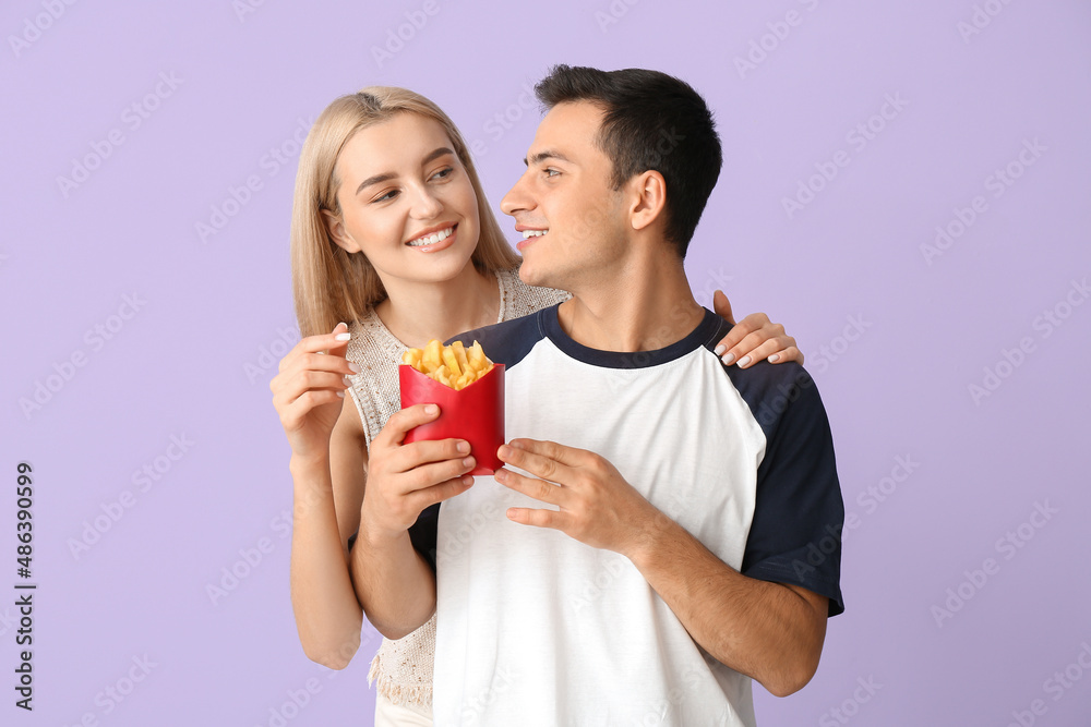 Young couple eating french fries on purple background