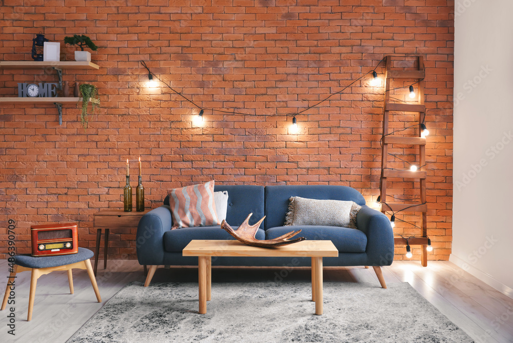 Stylish interior of living room with grey sofa and brick wall