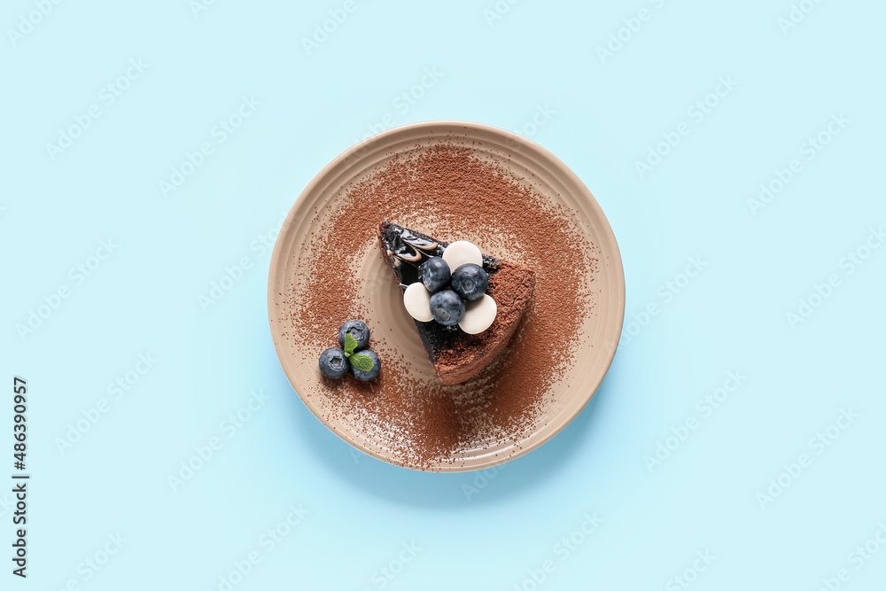 Plate with delicious piece of chocolate cake and blueberries on blue background