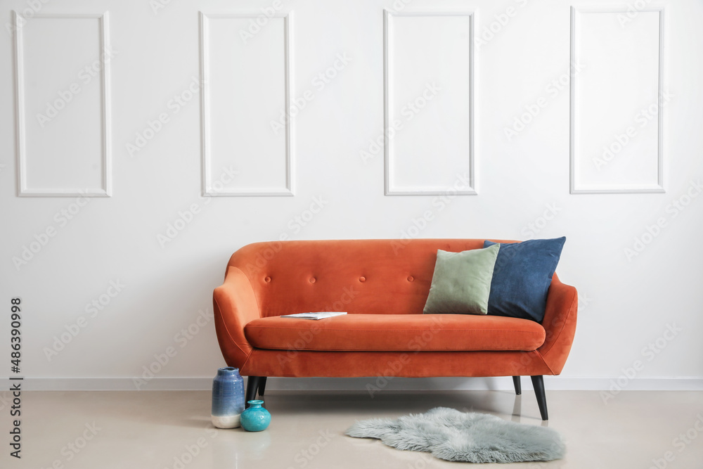 Stylish brown sofa with pillows, vases and rug near light wall