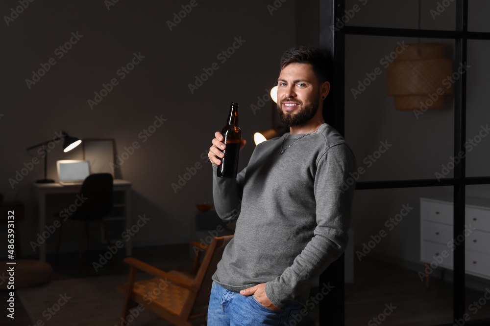 Young bearded man with bottle of beer at home in evening