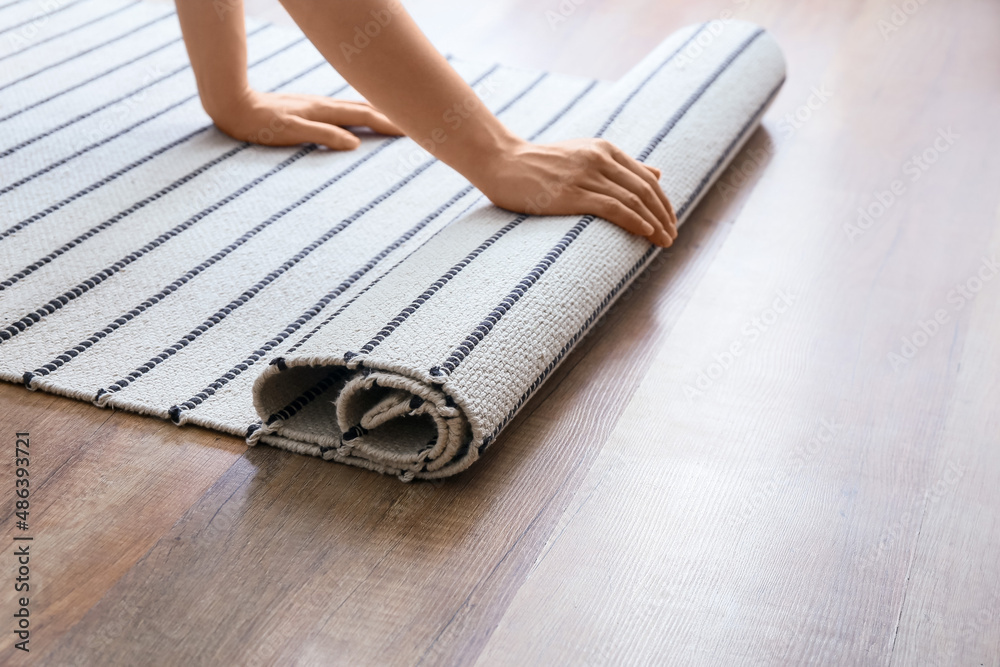 Woman rolling striped carpet on wooden floor