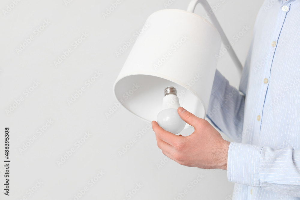 Woman changing light bulb in standard lamp near light wall, closeup