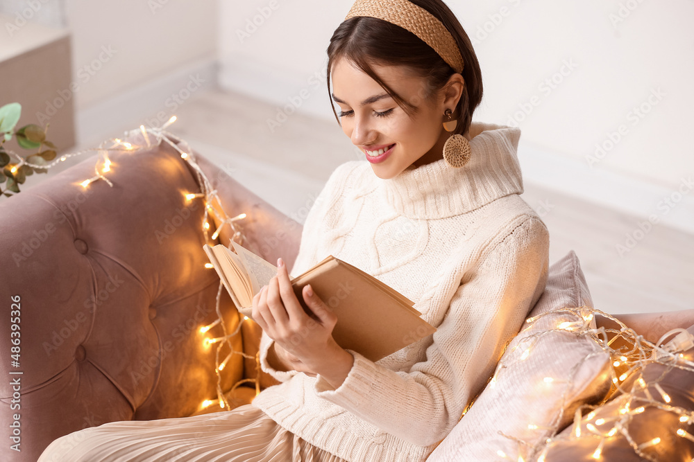 Beautiful young woman reading book on sofa at home