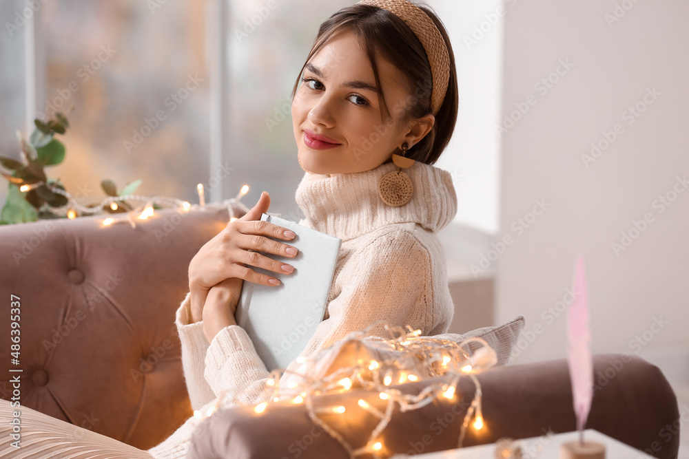 Beautiful young woman with book on sofa at home