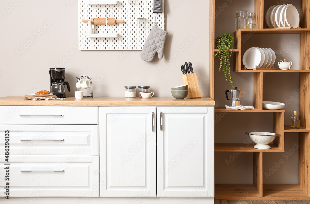 Interior of light kitchen with wooden shelving unit and pegboard