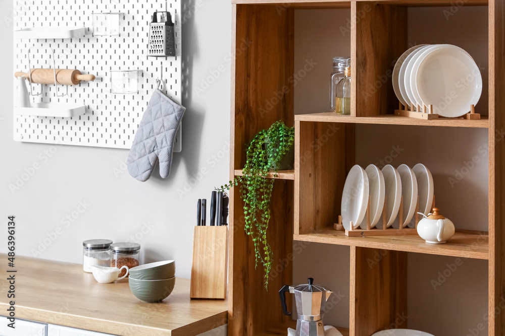 Wooden shelving unit with dishware, coffee maker and houseplant near light wall in kitchen