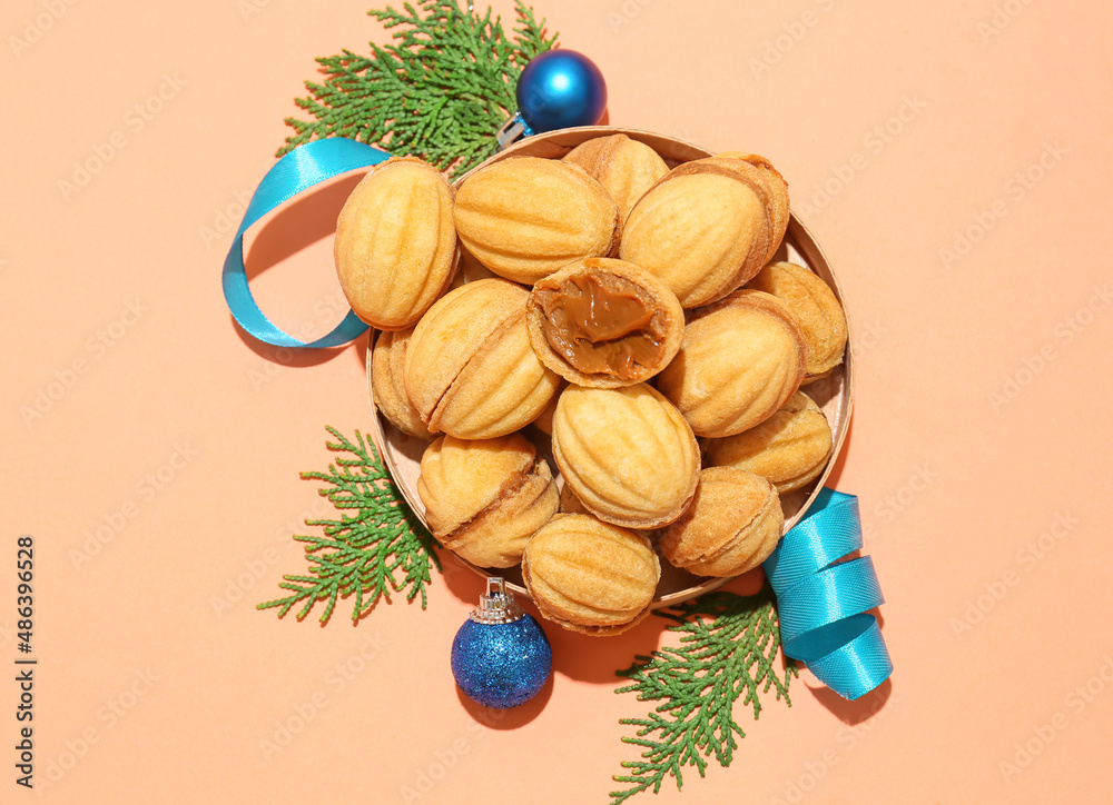 Bowl of tasty walnut shaped cookies with boiled condensed milk and Christmas decorations on color ba