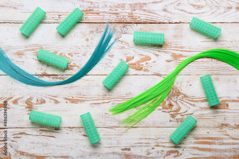 Green hair strands with curlers on light wooden background