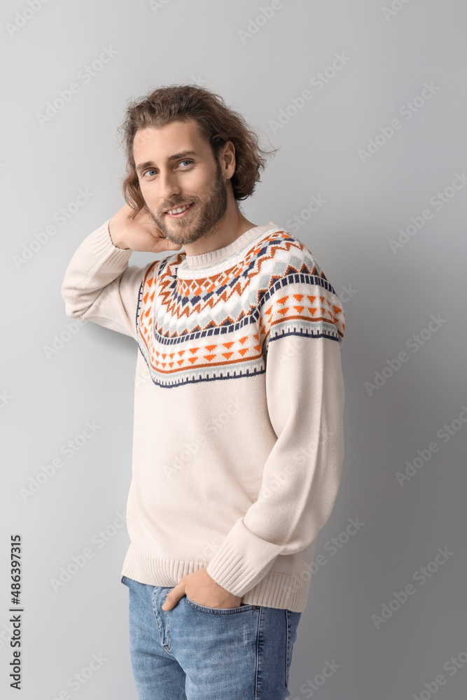 Handsome young man in knitted sweater on grey background