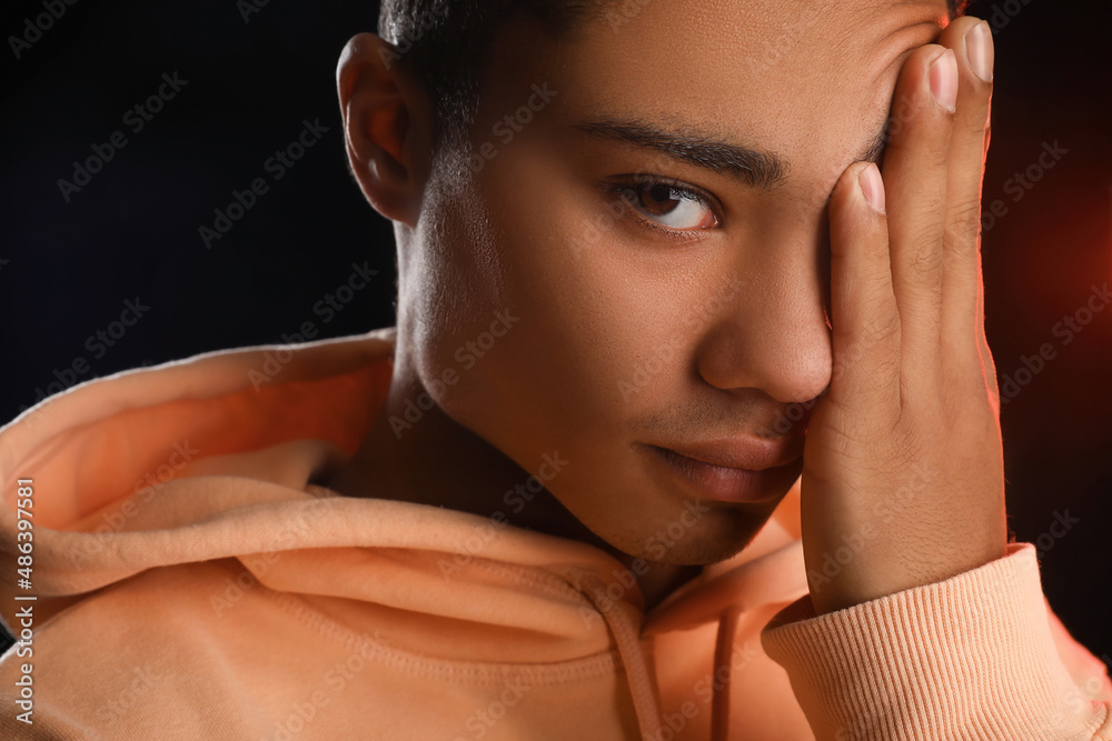 Tired African-American teenage boy in hoodie on black background, closeup