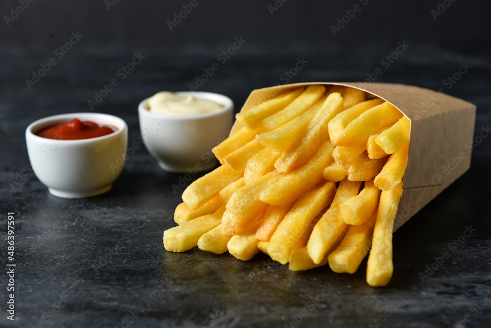 Paper box with tasty french fries on black background