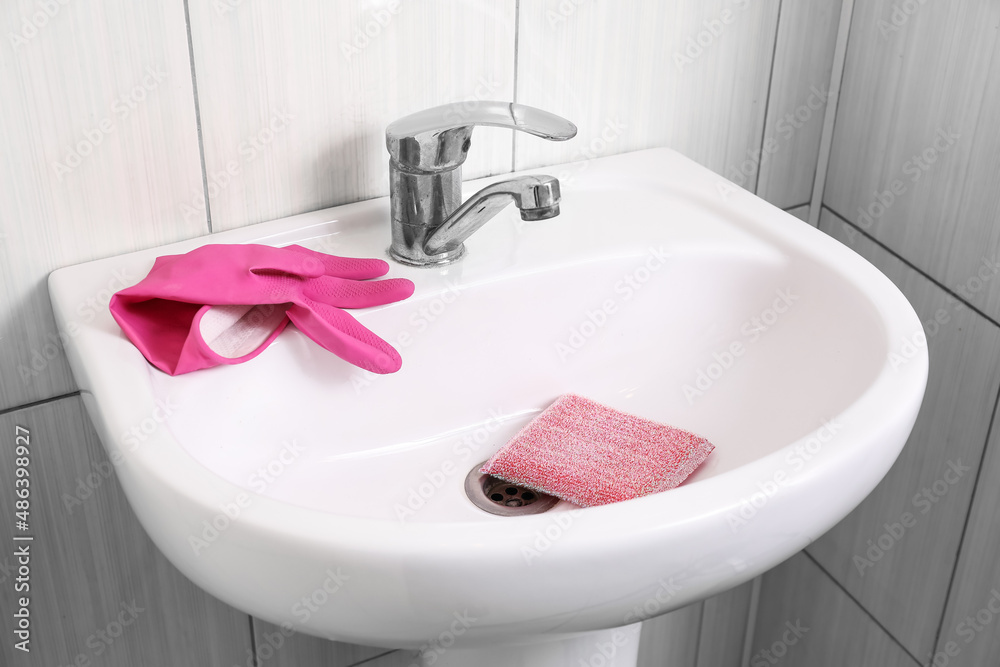 Modern sink with cleaning sponge and rubber glove in bathroom