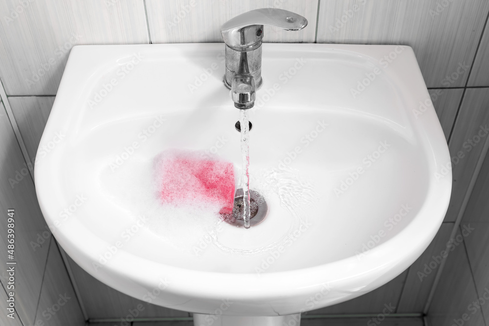 Modern sink with water, cleaning sponge and foam in bathroom