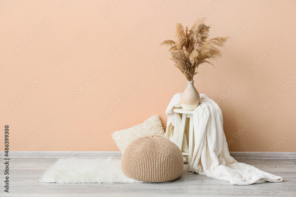 Table with vase, blanket and pouf near beige wall