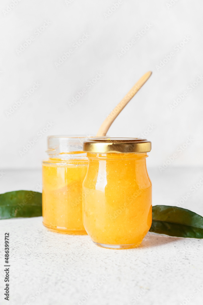 Glass jars of tasty orange jam on light background