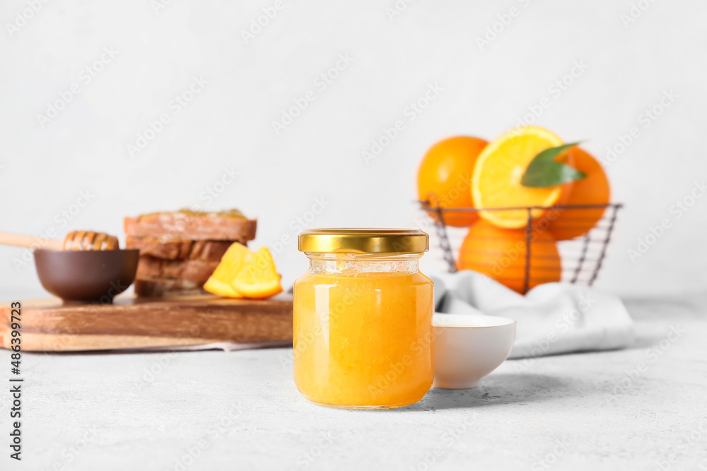 Glass jar of tasty orange jam on light background