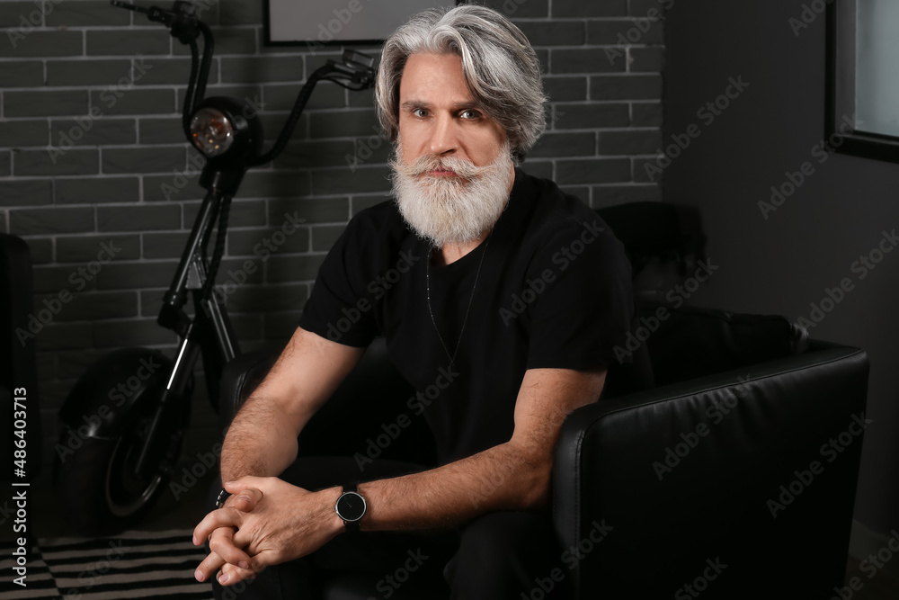 Portrait of handsome mature bearded man sitting in armchair at home