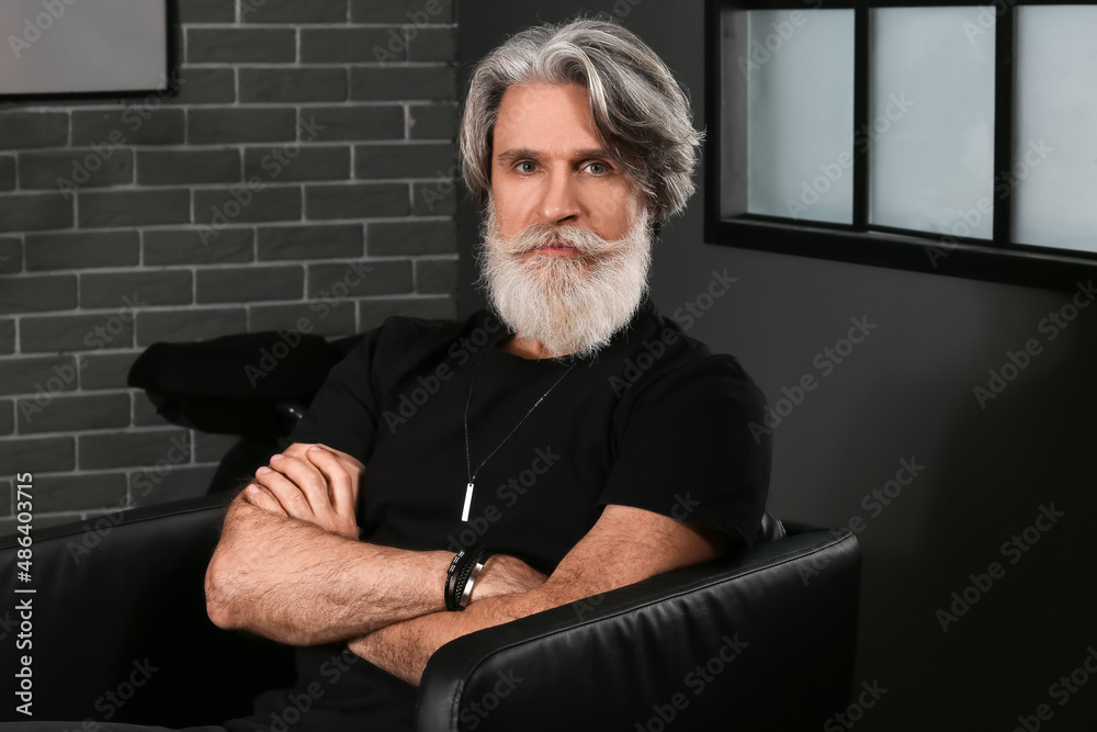 Portrait of handsome mature bearded man sitting in armchair at home