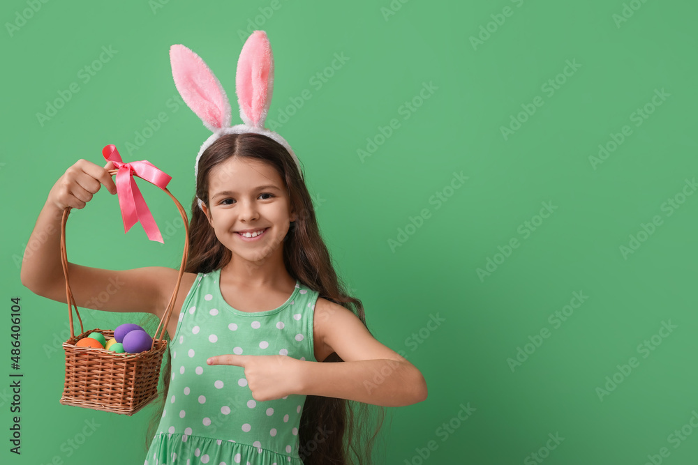 Cute little girl with bunny ears and Easter basket on green background