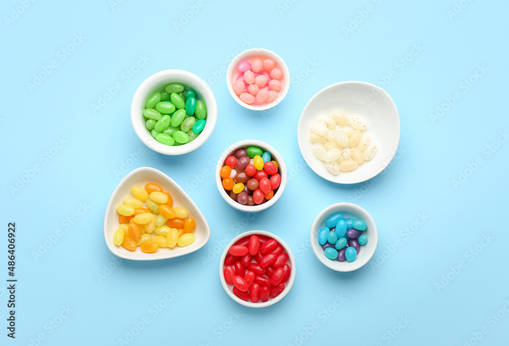 Bowls with different jelly beans on blue background