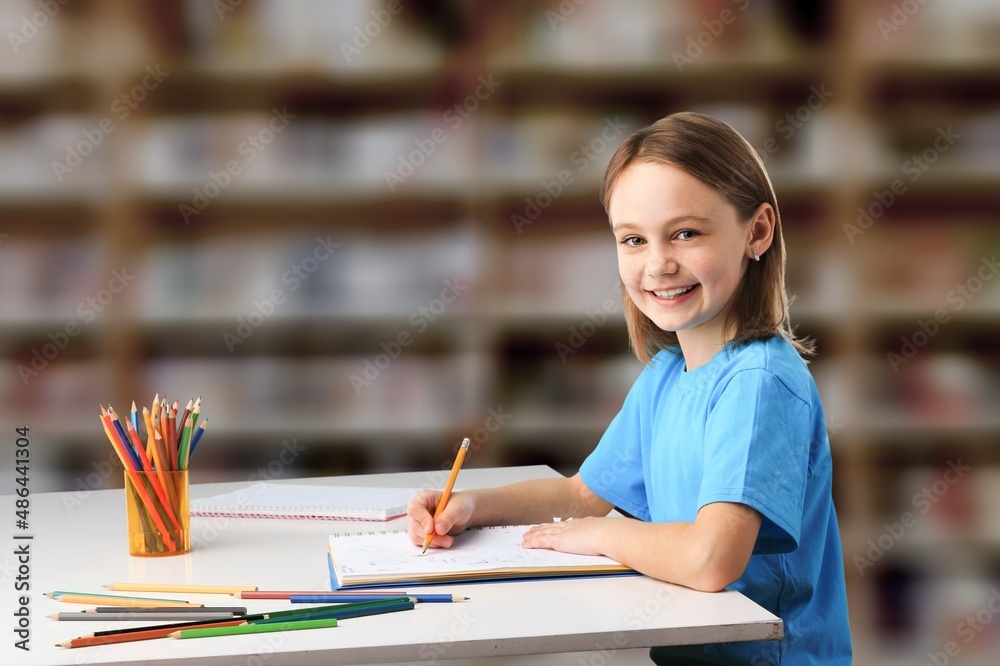 Happy schoolgirl sitting at desk, classroom background