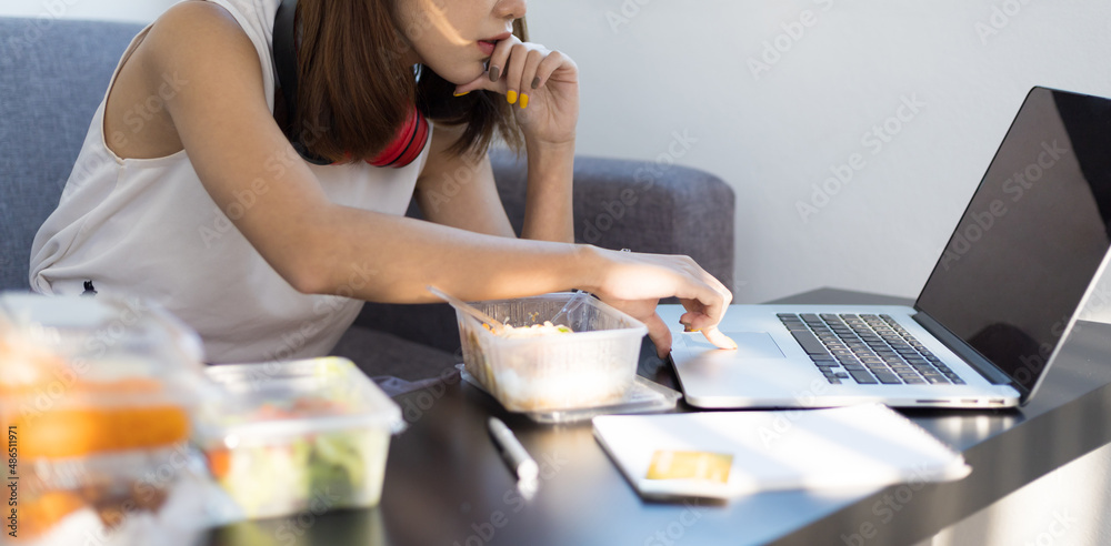 女性白天在家用笔记本电脑工作时吃午饭。在家工作和保持社交距离