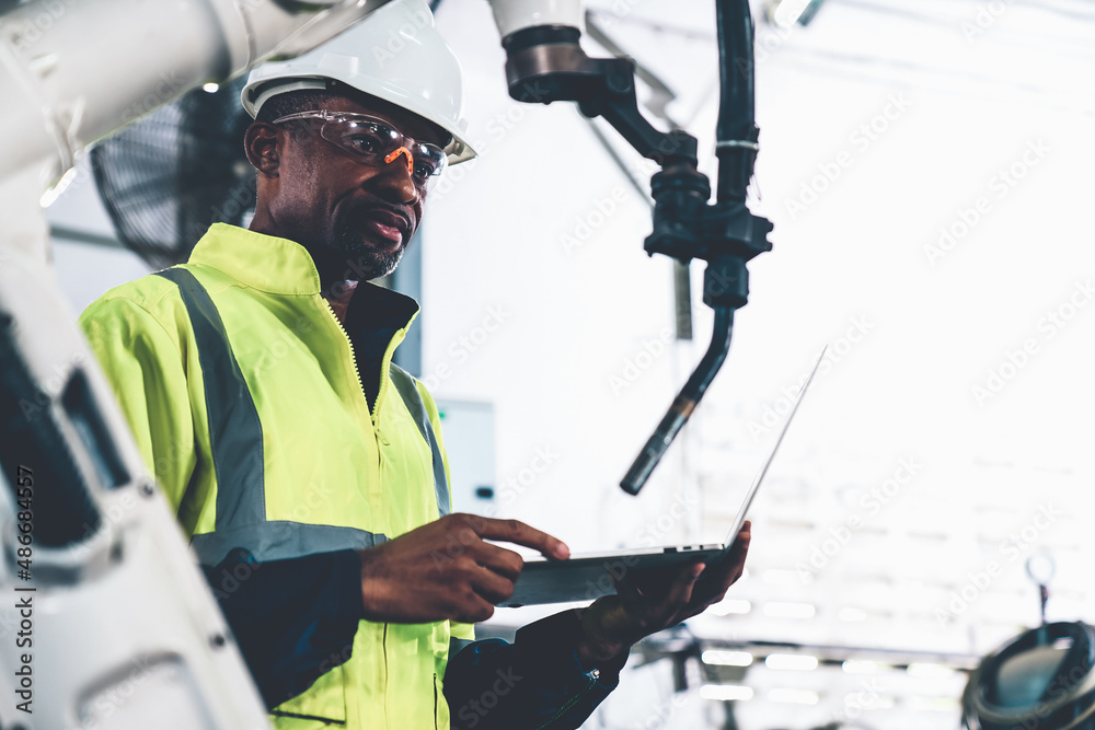 African American factory worker working with adept robotic arm in a workshop . Industry robot progra