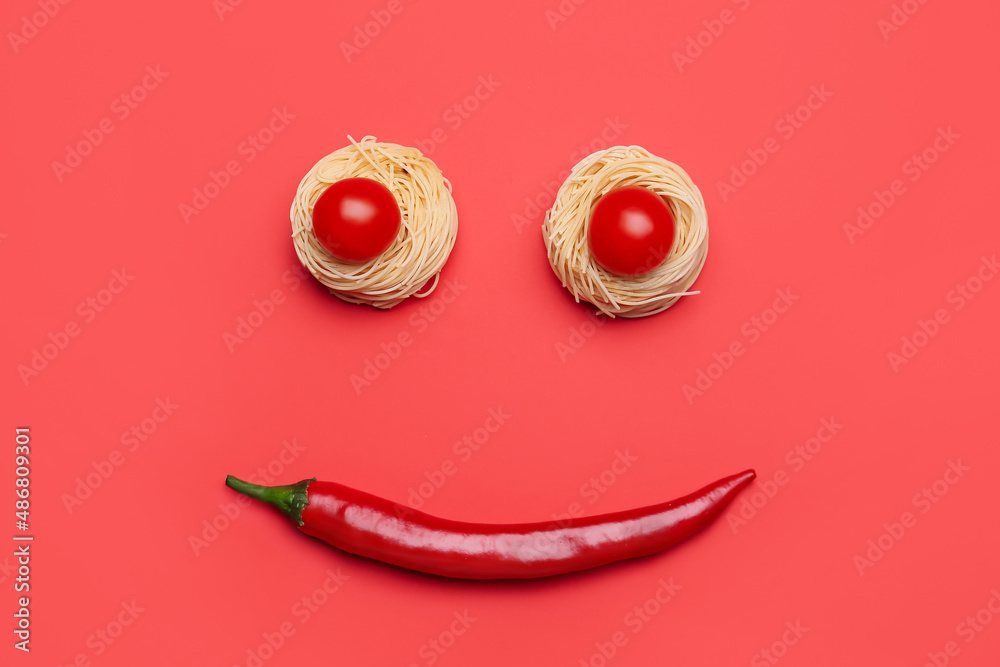 Smile made of hot chili pepper, pasta and tomatoes on red background