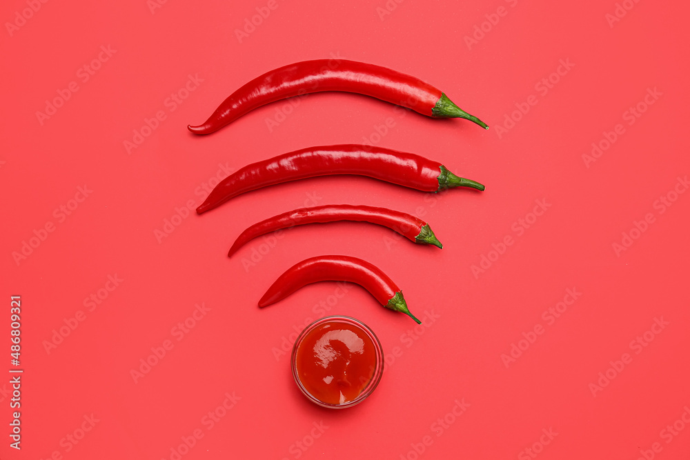 Hot chili peppers and bowl with sauce on red background