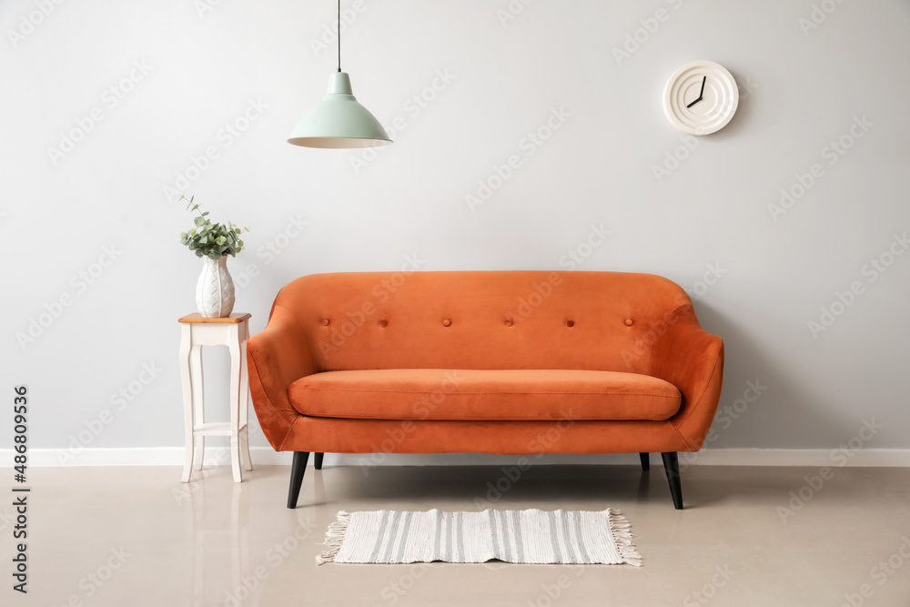 Stylish brown sofa and table with vase near light wall