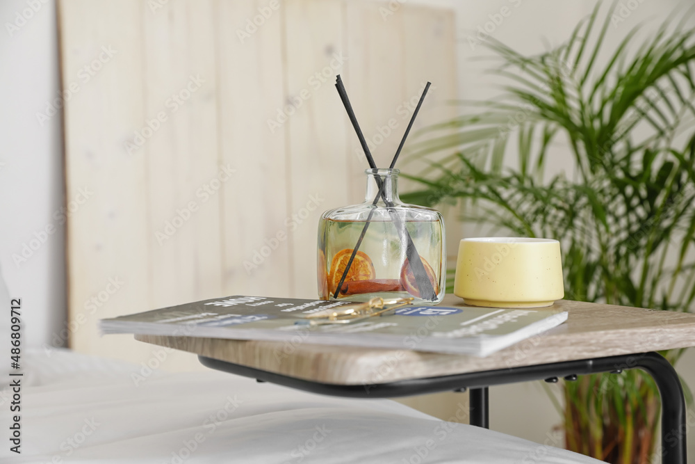 Aroma reed diffuser with magazine and cup on table in bedroom