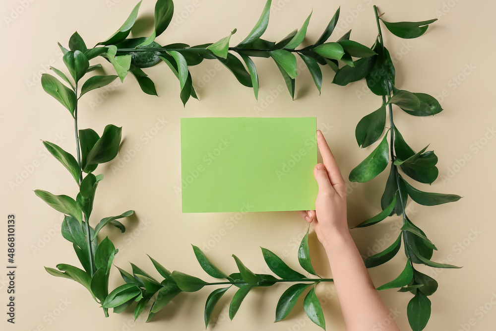 Female hand with blank card and fresh plant branches on color background