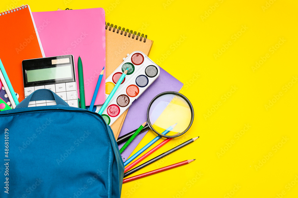 Backpack with different stationery on yellow background, closeup